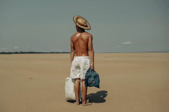 A photo of a shirtless man wearing white shorts stood on a beach