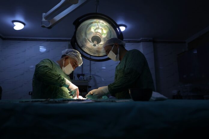 Two surgeons in scrubs and masks performing surgery in a dimly lit hospital operating room
