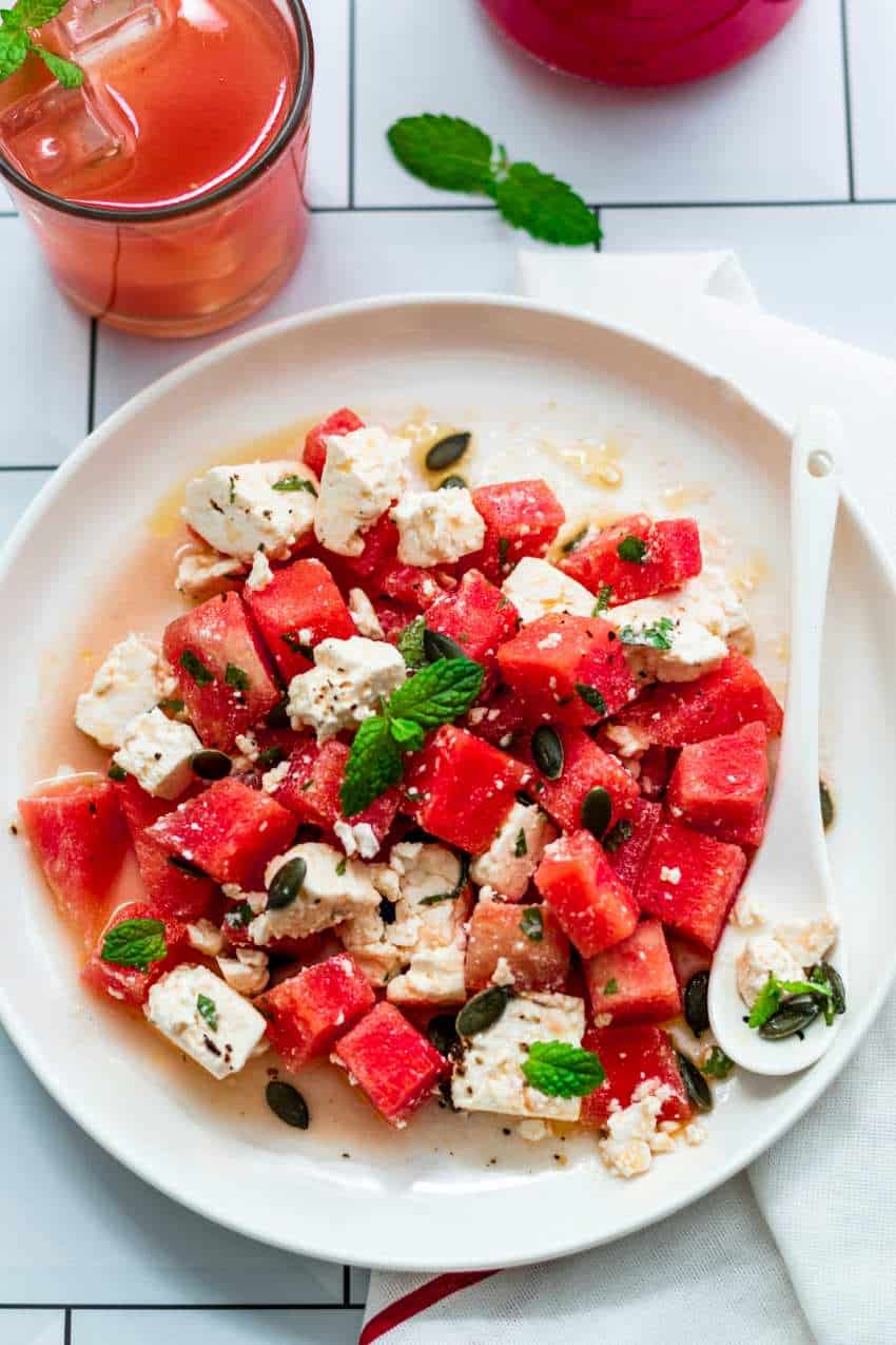A plate of watermelon salad, featuring chunks of ripe watermelon and cubes of feta cheese, garnished with sprigs of fresh mint leaves