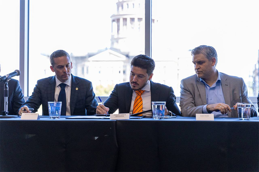 Three men sit at a table and sign a document