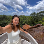 Nellie Huang, a woman with a tattoo of the world map on her arm takes a selfie in a Yucatán Peninsula forest.