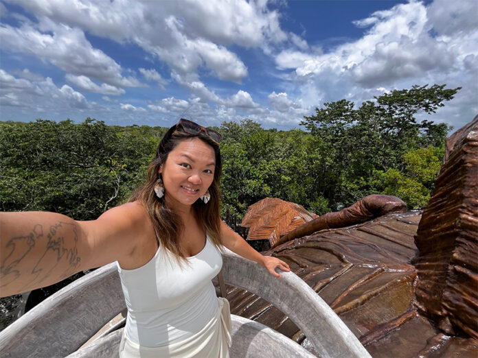 Nellie Huang, a woman with a tattoo of the world map on her arm takes a selfie in a Yucatán Peninsula forest.