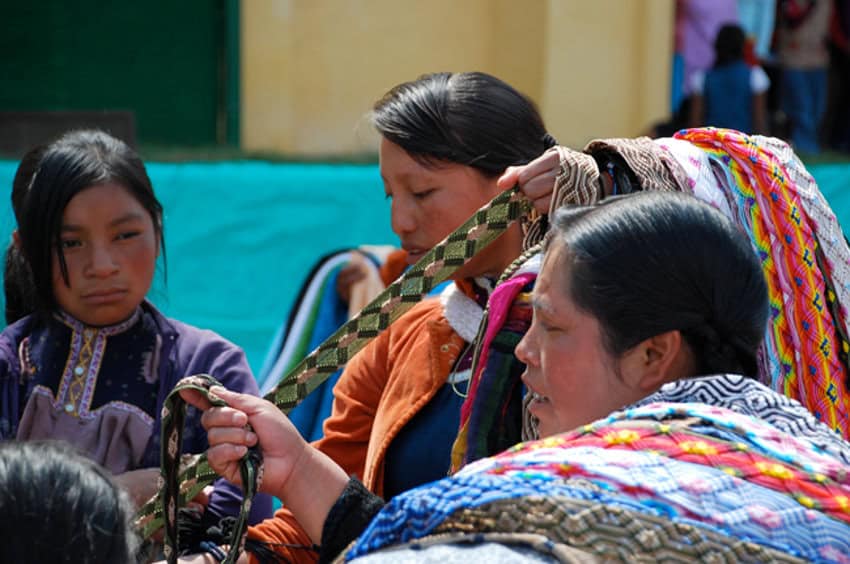 Three Indigenous women in San Cristobal de las Casas selling traditionally woven clothing items.