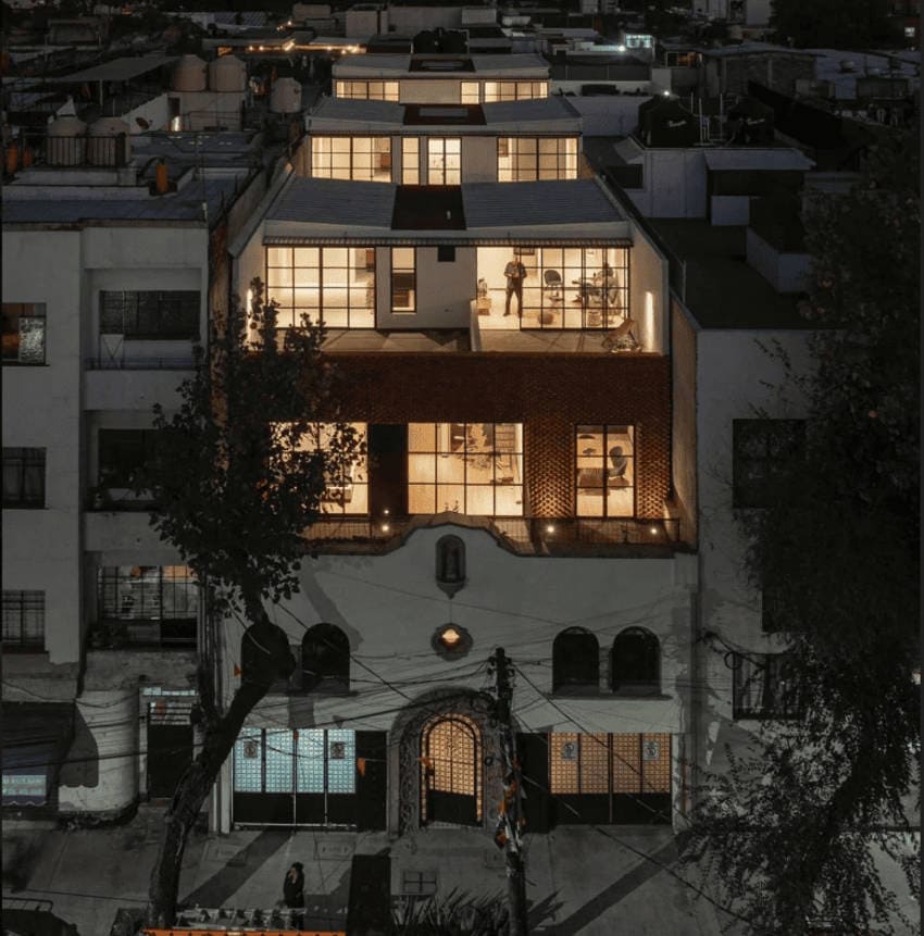 A multistory building in Mexico City at night, with warm light spilling from its many windows, illuminating modern interiors.