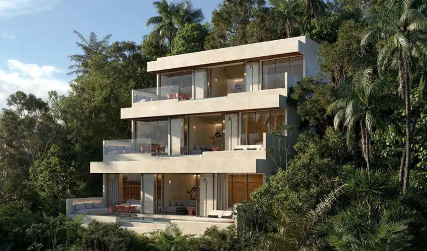 A modern, multi-story villa with large glass windows and balconies is nestled into a lush green hillside surrounded by dense tropical foliage and palm trees.