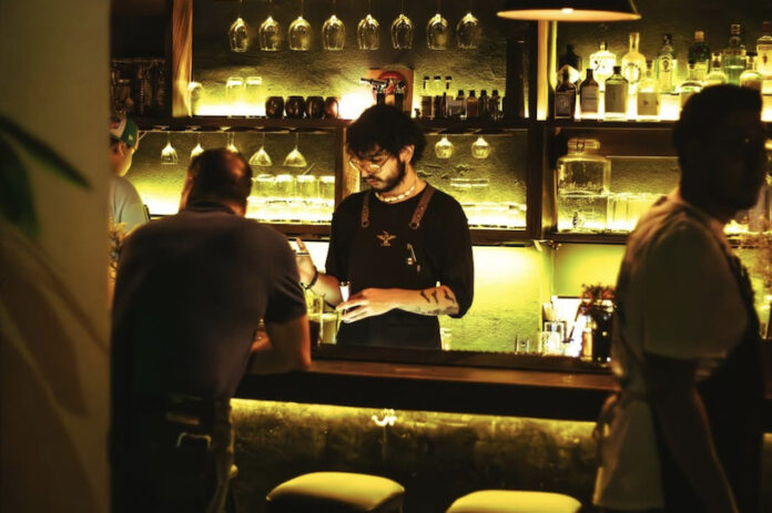 A barman makes cocktails in a green-lit bar, one of puerta vallarta bars best spots.