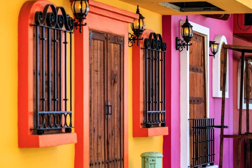 House facades on a street painted in different bright cheery colors with picturesque black wrought iron grids over many doors and windows and retro lamps made to look like gas lamps.