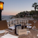 What’s on in Los Cabos in August? A reserved table at an outdoor restaurant overlooks a beach and ocean at sunset in Los Cabos, Baja California Sur, Mexico