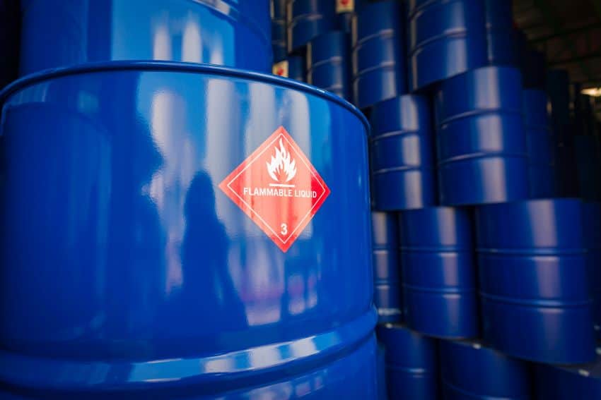 Blue barrels of oil stacked high in rows. One in front has a sticker saying "flammable liquid" on it.