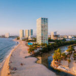 Where and why to find the last bastions of Puerto Vallarta’s history Aerial view of modern high-rise resorts and condominiums lining the sandy beach and coastline of Puerto Vallarta, Mexico, with Banderas Bay stretching into the distance.