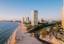 Aerial view of modern high-rise resorts and condominiums lining the sandy beach and coastline of Puerto Vallarta, Mexico, with Banderas Bay stretching into the distance.