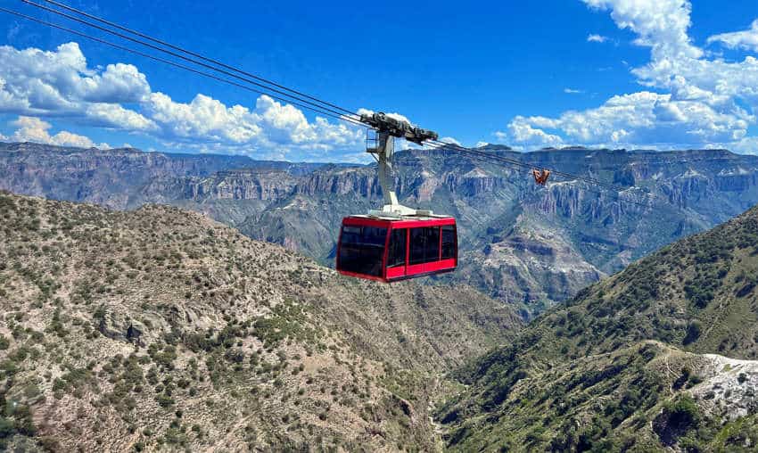 A sunlit panoramic view of Copper Canyon, with a cable car full of tourists capturing moments against the sprawling natural vista, under a nearly clear sky, with no identifiable traces of individuals