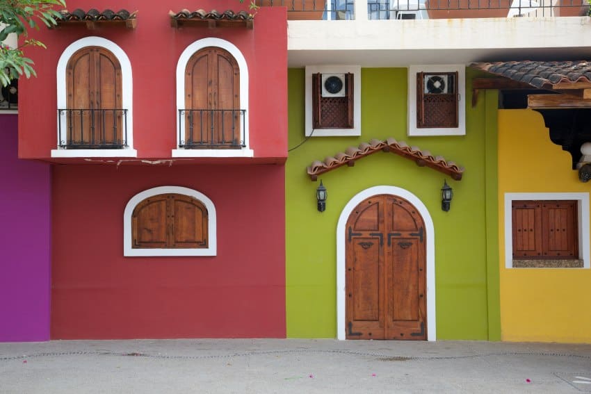 The facades of three brightly colored Mexican adobe homes with window balconies in wrought iron.