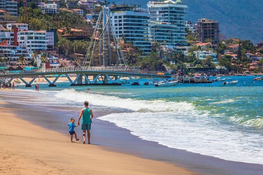A father walking on a PV beach with buildings in the background