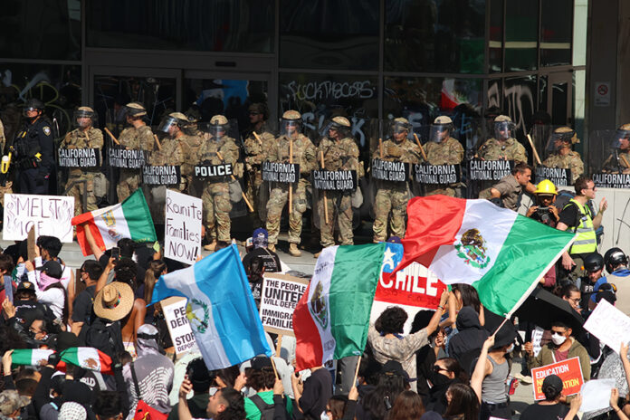 Protesters with Mexican flags and signs stand in front of a wall of California National Guard troops