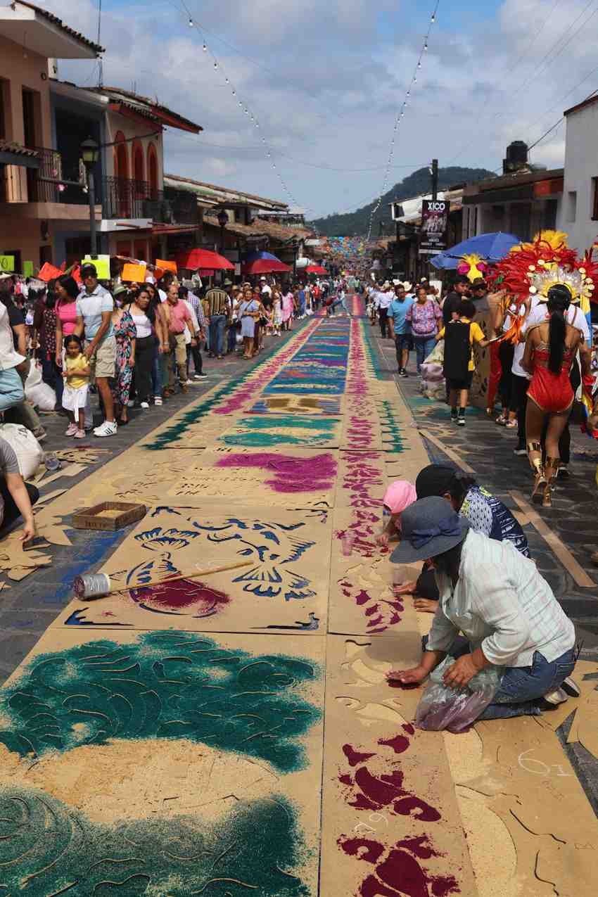 Community members create elaborate "tapetes" — colorful sawdust carpets with intricate floral and geometric patterns — stretching down Xico's main street during La Xiqueñada festival.