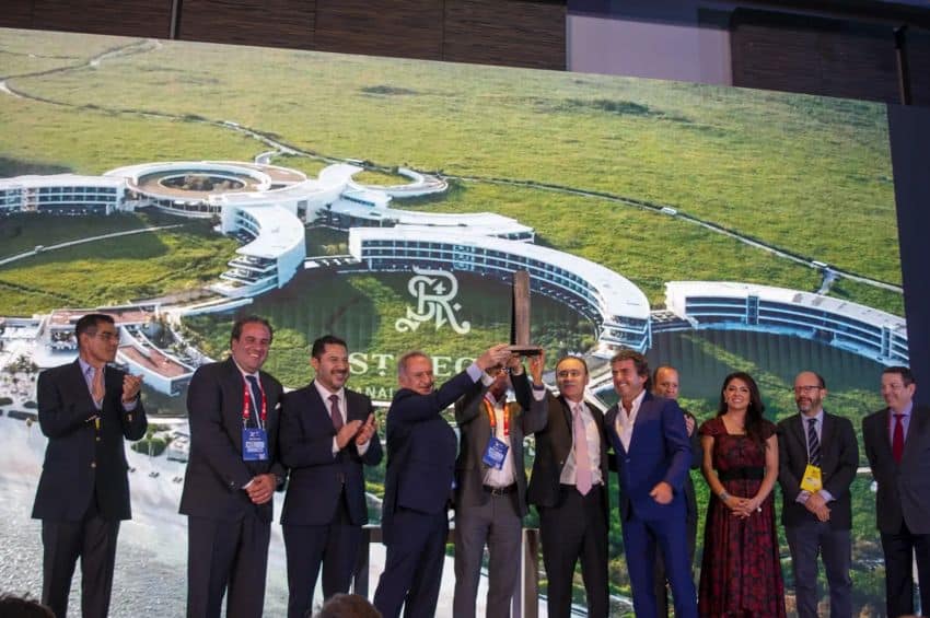 A group of people on a stage holding up what appears to be a trophy made of wood to look like a skyscraper.