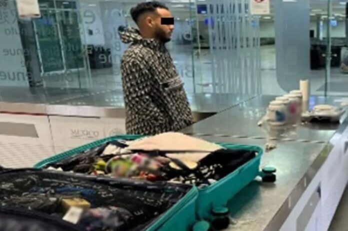 A man stands by an open suitcase in an airport revision area