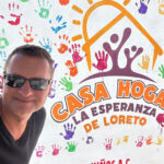 A man in sunglasses in front of a building entrance sign reading Casa Hogar La Esperanza de Loreto