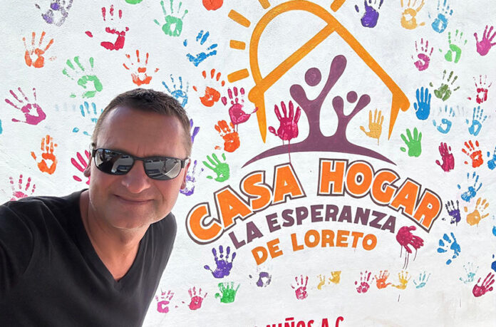 A man in sunglasses in front of a building entrance sign reading Casa Hogar La Esperanza de Loreto