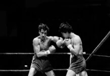 Tales from Mexico’s golden era of boxing: 1977’s ‘Battle of the Z Boys’ A black-and-white action shot of two boxers exchanging punches in a boxing ring. The boxer on the left, with a mustache and dark, messy hair, is throwing a left hook, while the boxer on the right is in a defensive or counterpunching stance. Both are wearing boxing gloves and shorts.