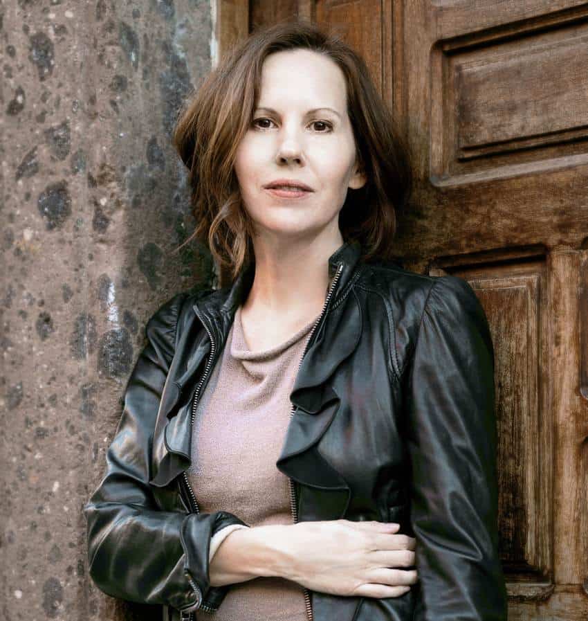 Author Danielle Trussoni standing against a wooden door and a cement wall looking at the camera.