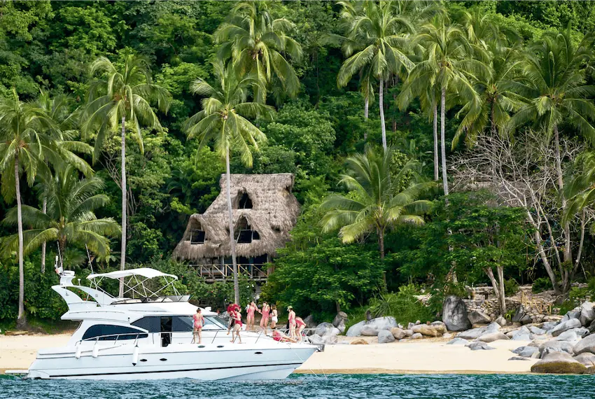 A yacht in front of a quiet sandy beach with a palapa